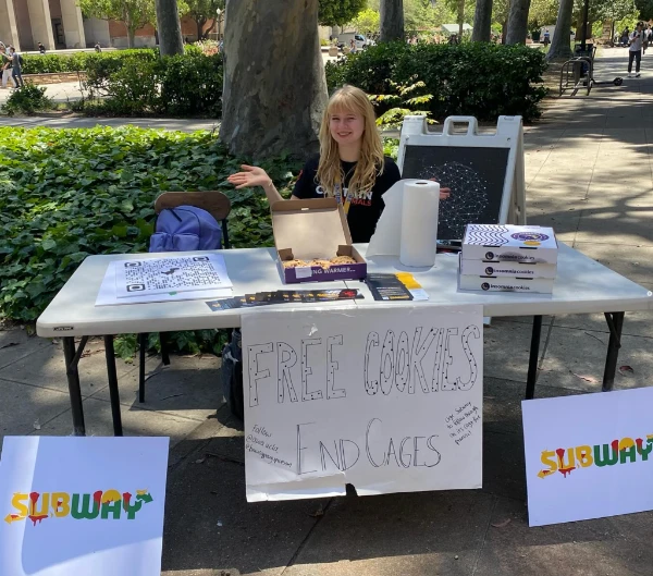A member tabling with free cookies and an End Cages sign